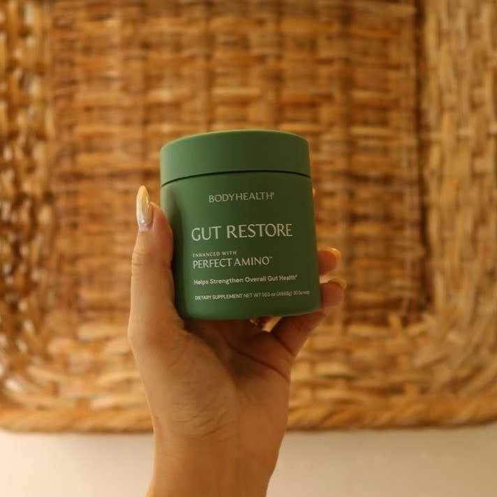 Hand holding a green container labeled 'Gut Restore' against a woven background
