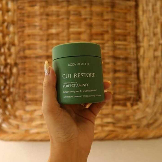 Hand holding a green container labeled 'Gut Restore' against a woven background